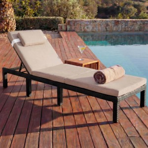 Anthrazitfarbene Poly-Rattan Sonnenliege mit creme-farbenen Kissen auf Holzdeck am Pool.