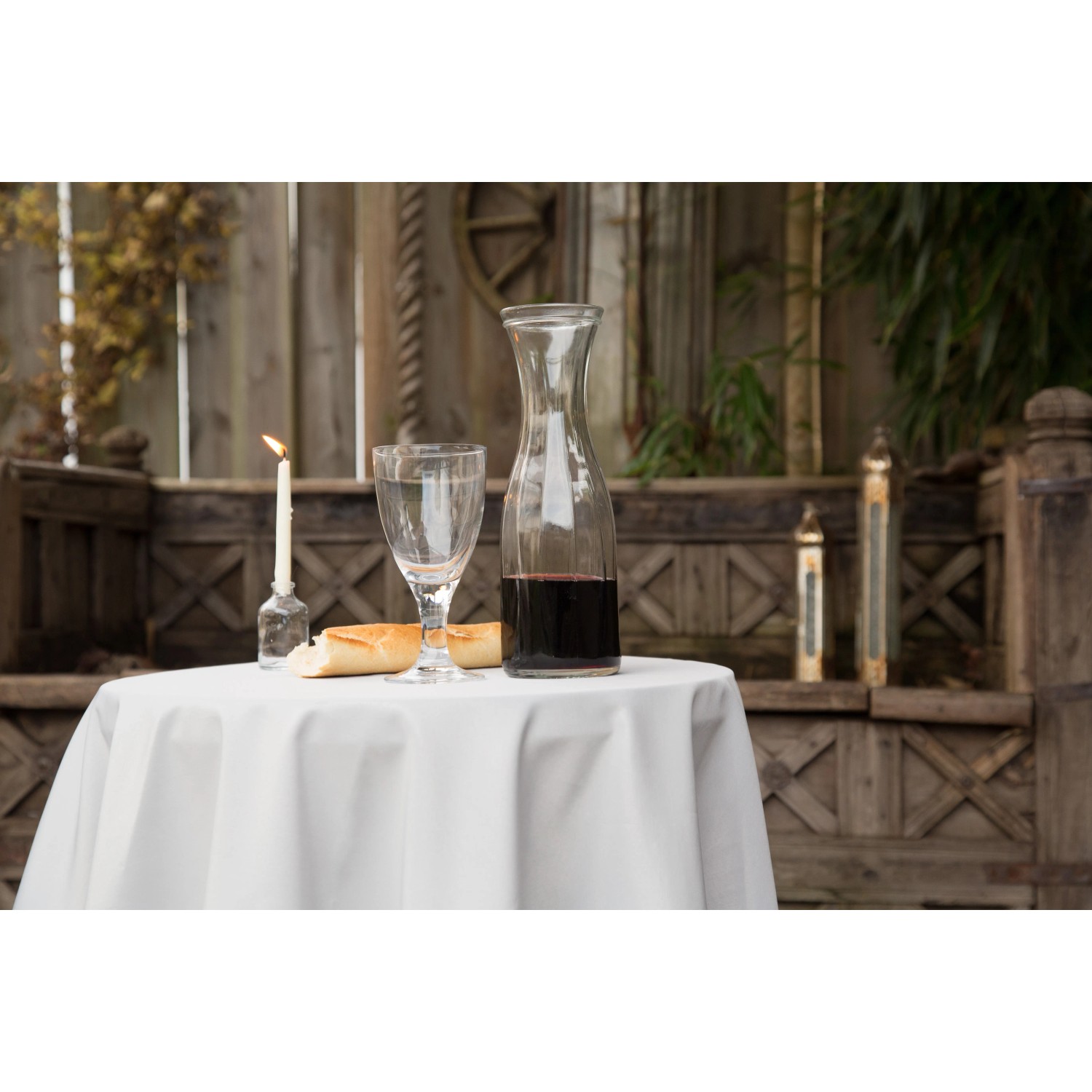 Gedeckter Tisch mit silbergrauer, runder Floracord Tischdecke (160 cm), Karaffe, Glas, Brot und Kerze.