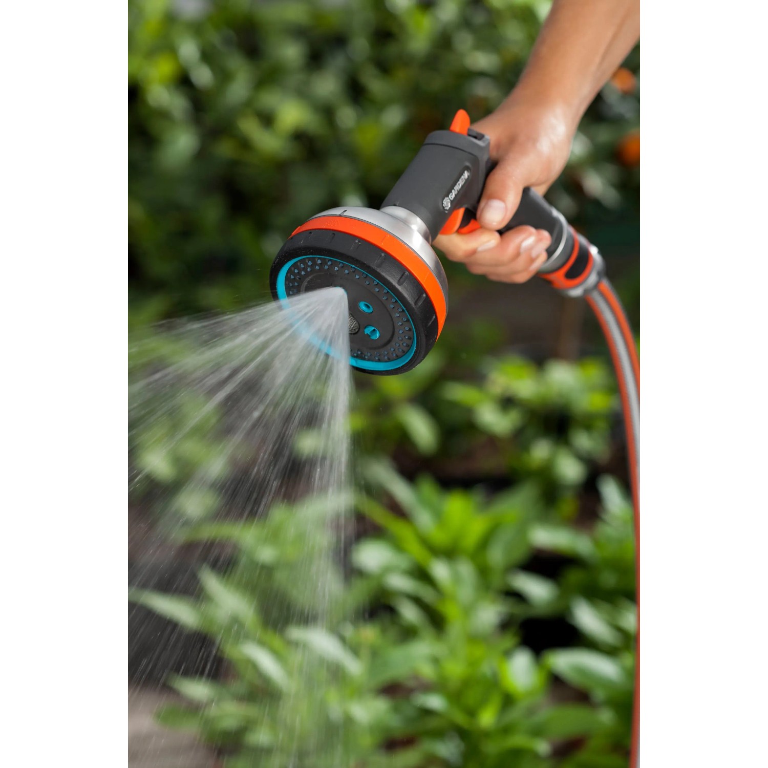 Gardena Premium Multibrause in Aktion: Hand hält Gartenspritze mit Wasserstrahl vor grünem Hintergrund.
