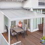 Weiße Gutta Terrassenüberdachung mit Polycarbonatplatten und sitzender Person am Tisch.