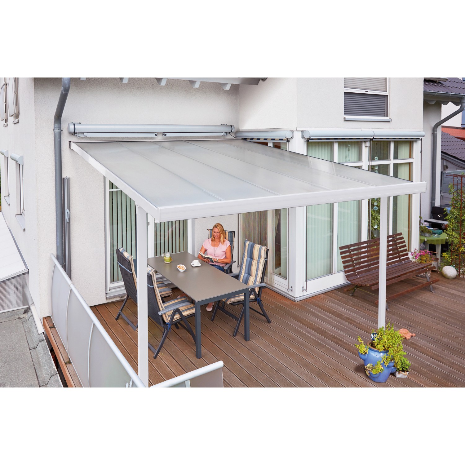 Weiße Gutta Terrassenüberdachung mit Polycarbonatplatten und sitzender Person am Tisch.