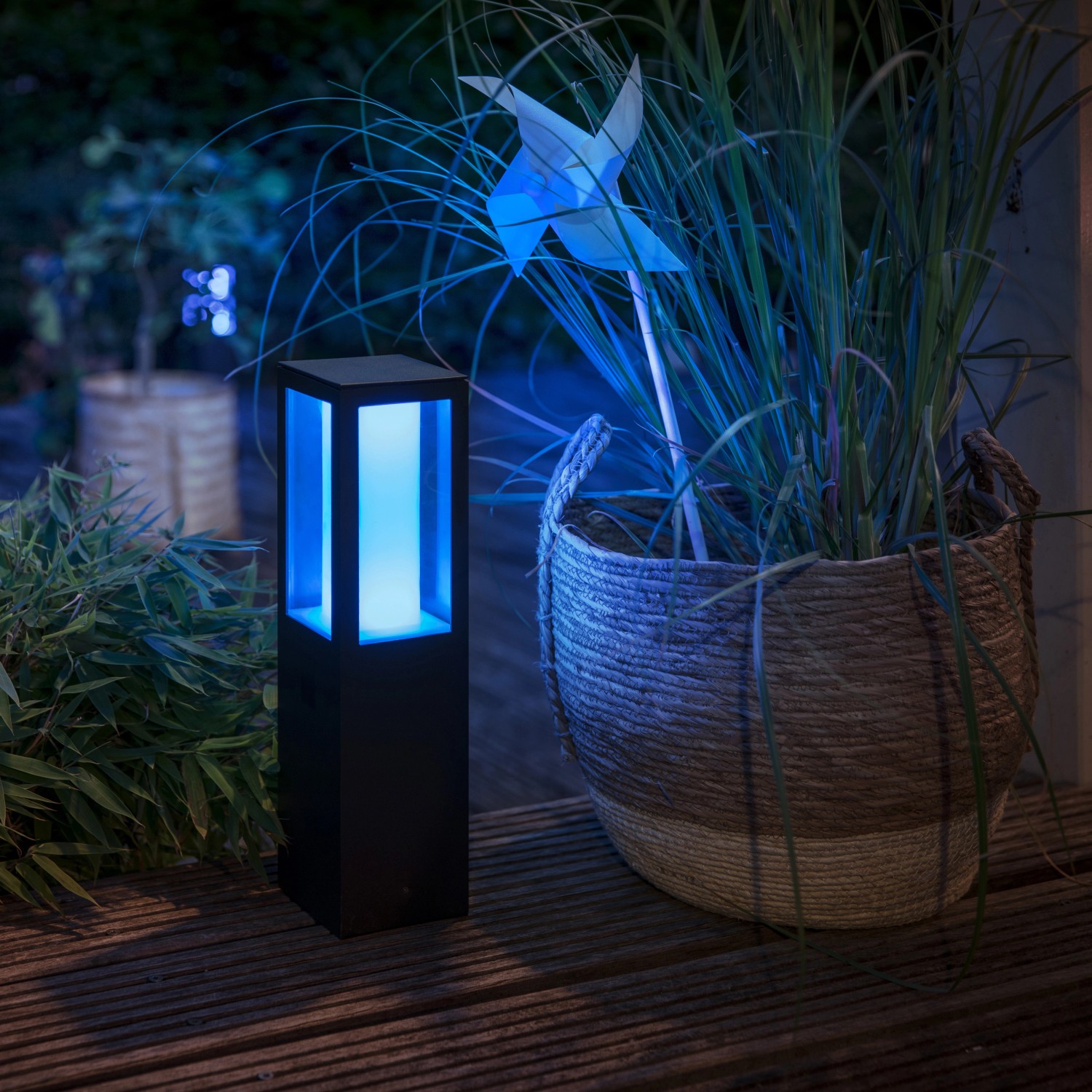 Philips Hue Impress Sockelleuchte, smarte LED Außenleuchte mit blauem Licht neben Pflanze im Korb.