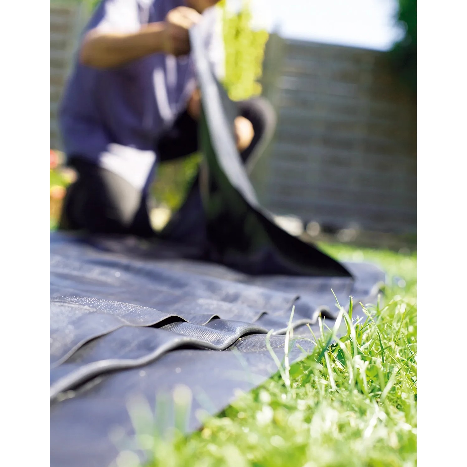 Schwarze Heissner PVC Teichfolie (6x6m) wird im Garten verlegt.