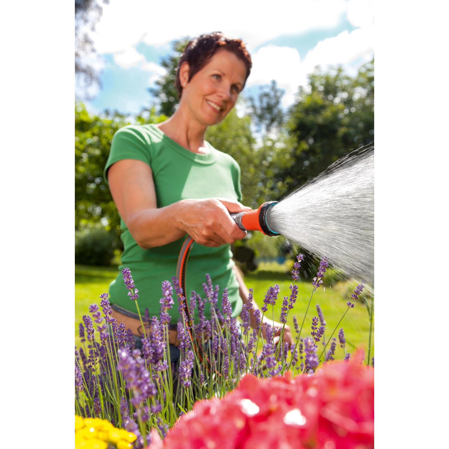 Frau bewässert Blumen mit Gardena Bewässerungsbrause. Gartenspritze mit Wasserstrahl.