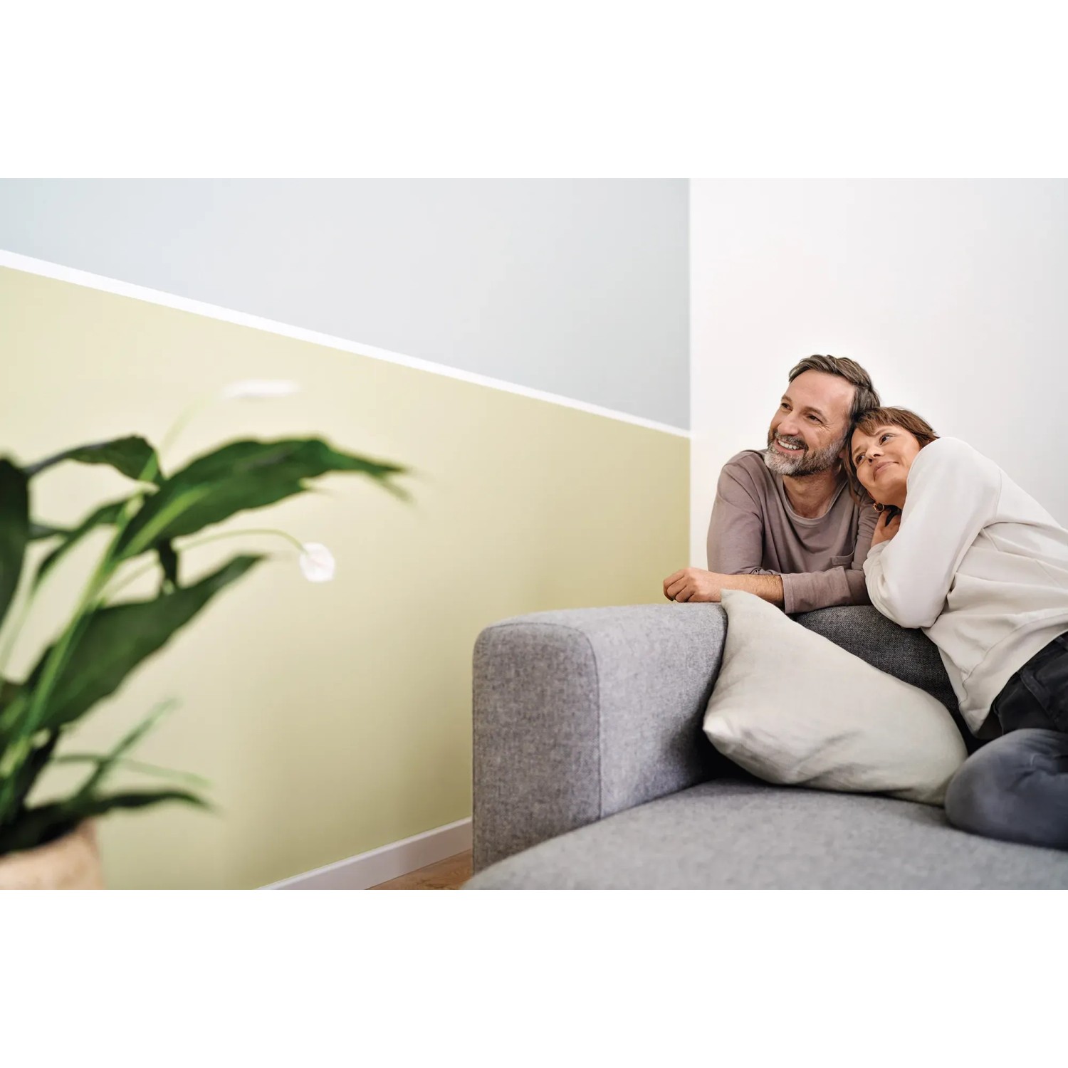 Paar entspannt auf Sofa vor Wand mit Tesa Malerband abgeklebt. Für präzise Farbkanten.