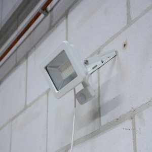 Weißer LED-Außenstrahler mit Sensor (30W, 3300lm, 4000K) an einer Wand montiert.