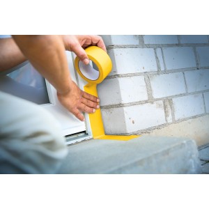 Anwendung von gelbem LUX Putzerband zum Abdecken von Fensterrahmen und Mauerwerk.