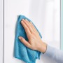 Hand wischt mit blauem Tuch eine glatte, weiße Oberfläche ab.