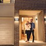 Silberne Ledvance Smart+ Brick Außenwandleuchte an einer Hauswand mit Paar vor der Haustür.