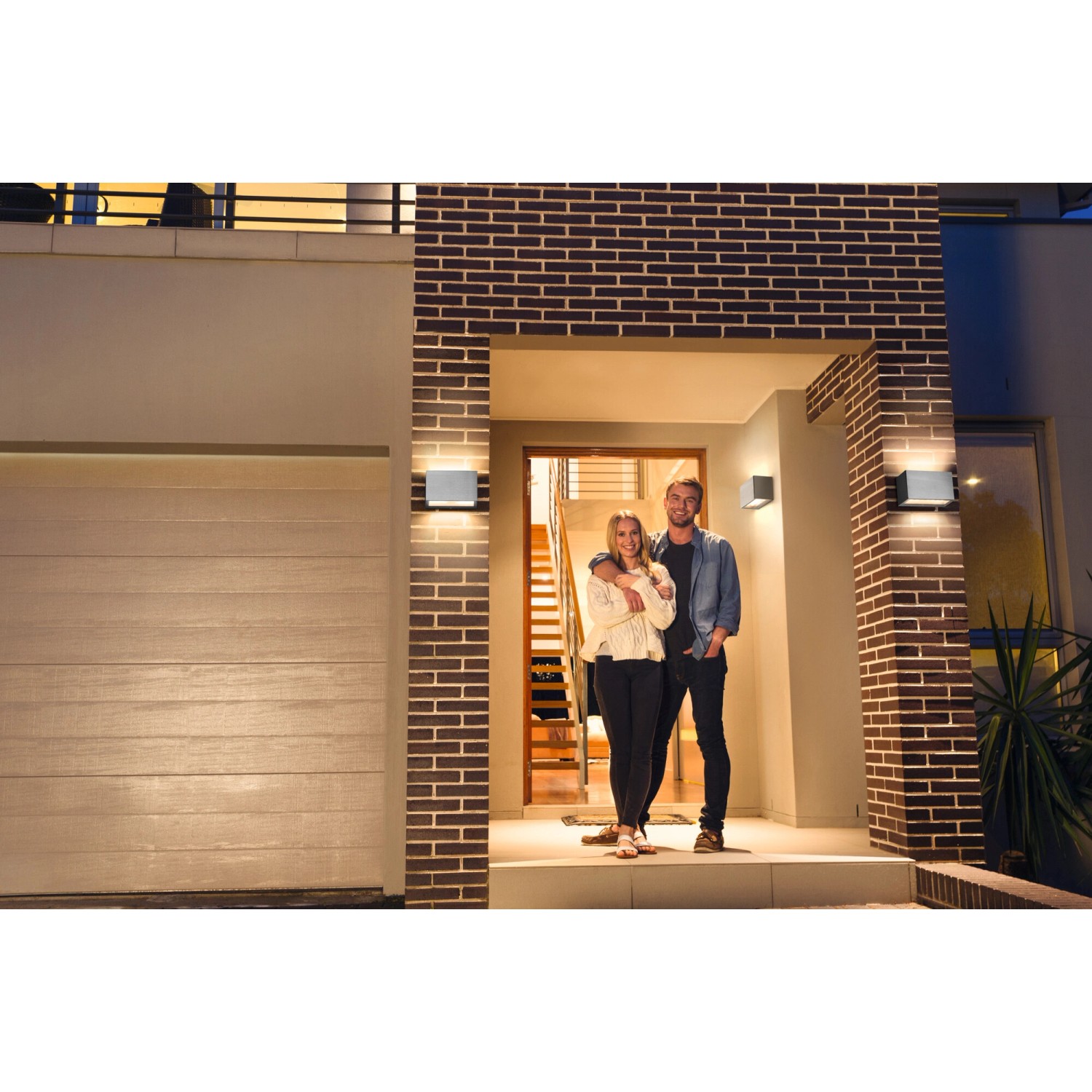 Silberne Ledvance Smart+ Brick Außenwandleuchte an einer Hauswand mit Paar vor der Haustür.