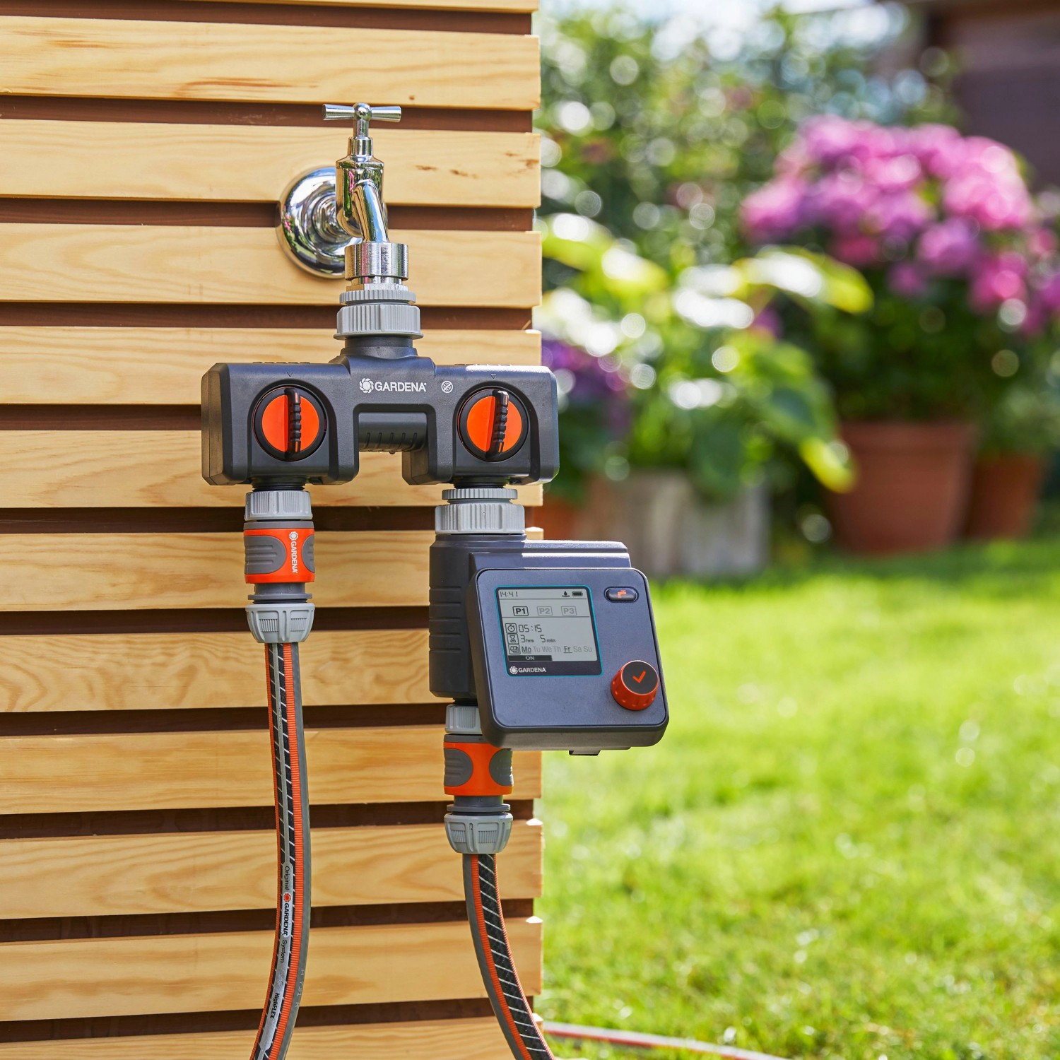 Gardena Bewässerungscomputer Select am Wasserhahn mit angeschlossenen Schläuchen im Garten.