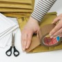Tesapack Strong Packband braun beim Verschließen eines Versandbeutels, mit Schere und weiteren Beuteln.