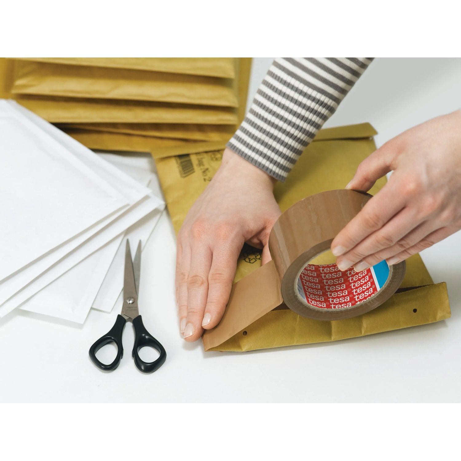 Tesapack Strong Packband braun beim Verschließen eines Versandbeutels, mit Schere und weiteren Beuteln.