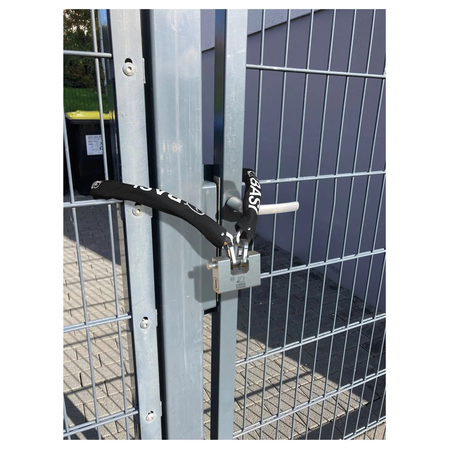 Basi Kettenschloss ZR 321: Schwarze ummantelte Stahlkette mit Blockschloss sichert ein graues Metalltor. Robustes Fahrradschloss.