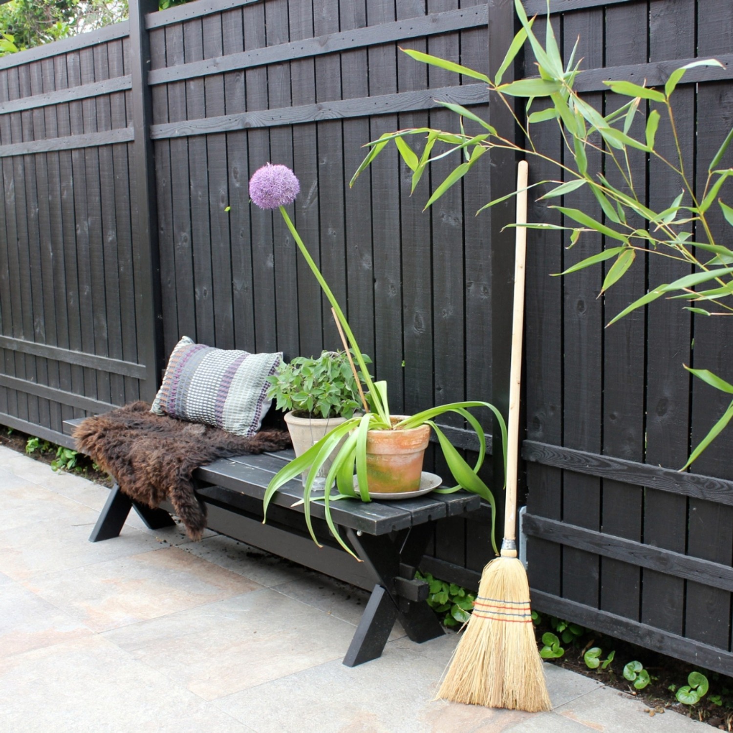 Schwarzer Sichtschutzzaun Rustik Nadelholz (180x180cm) mit Bank, Pflanzen und Besen im Garten.