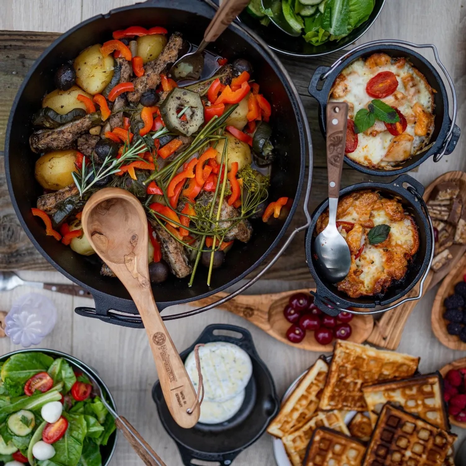 Petromax Dutch Oven FT9-T mit Speisen, Salaten und Waffeln auf einem Tisch. Grillutensil für Outdoor-Küche.
