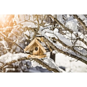Vogelfuttersilo Villa aus Holz mit Dach, hängt an verschneitem Ast. Vogelfutterspender für den Winter.