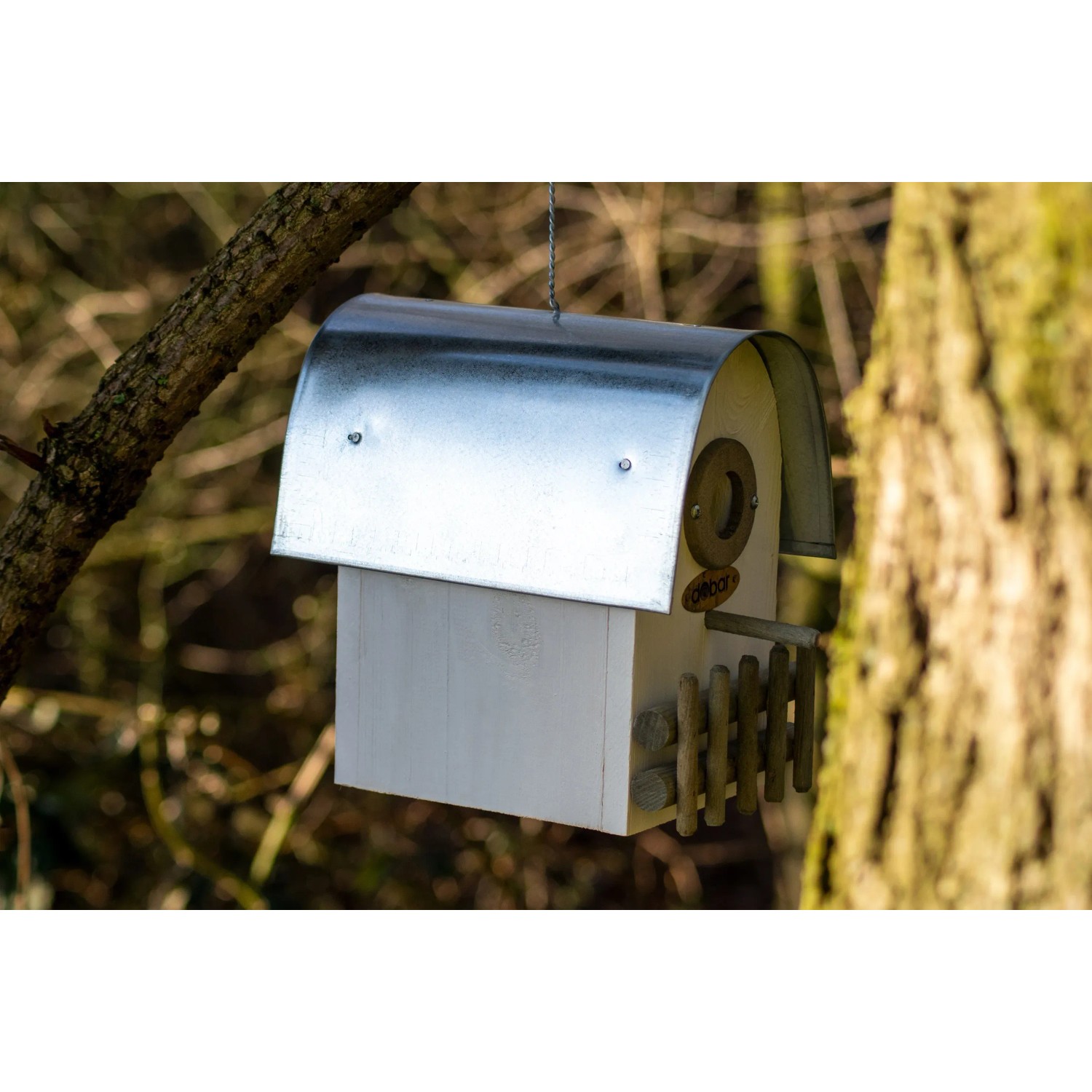 Elfenbeinfarbener Nistkasten „Rundhaus“ mit Alu-Dach, hängend an einem Baum.