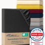Dunkelgraues Jersey Spannbettlaken aus Baumwolle, gefaltet, mit elastischem Rand. Im Hintergrund Stapel bunter Bettlaken. Made in Germany.