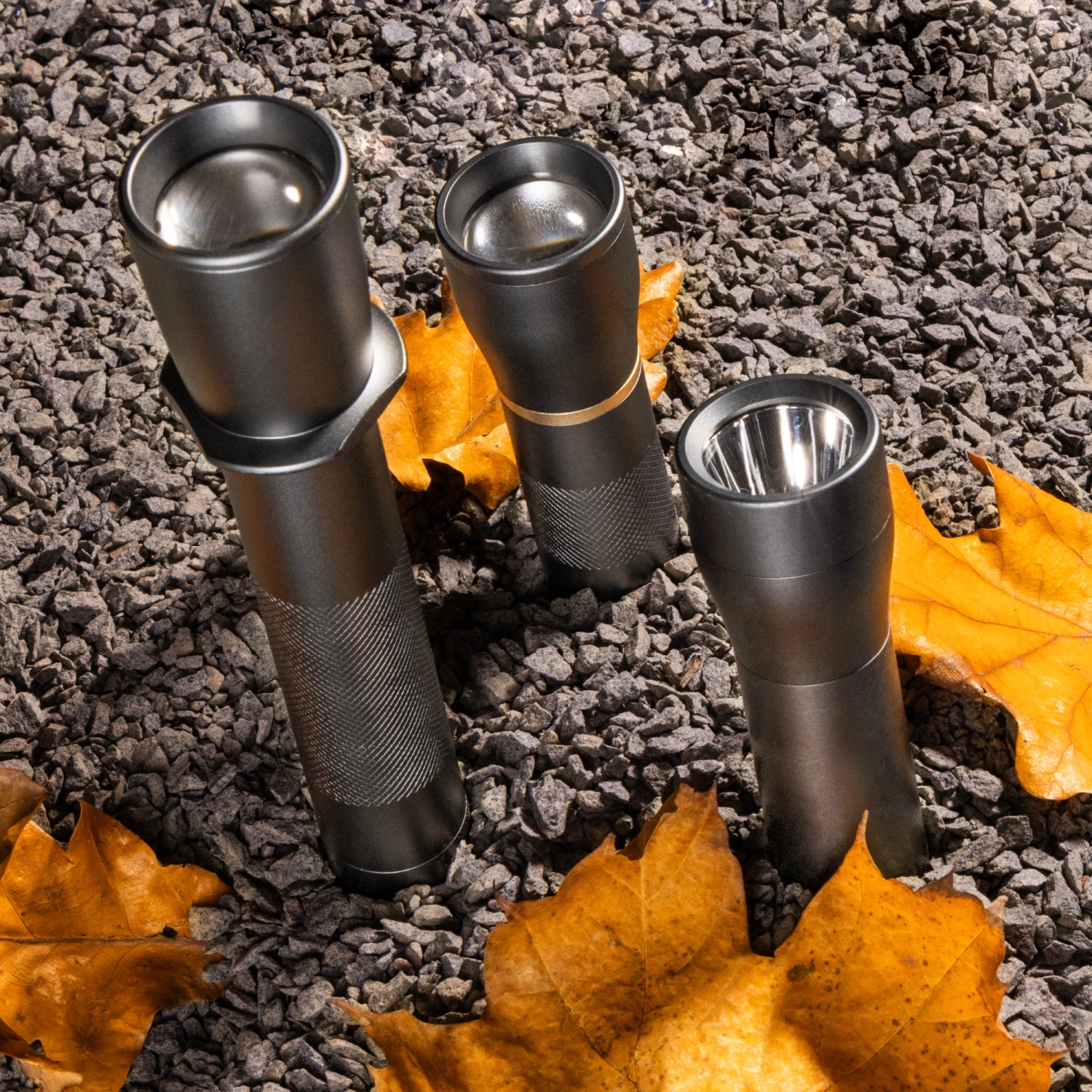 Drei dimmbare LED's Work Taschenlampen (900lm) auf Steinen mit Blättern.