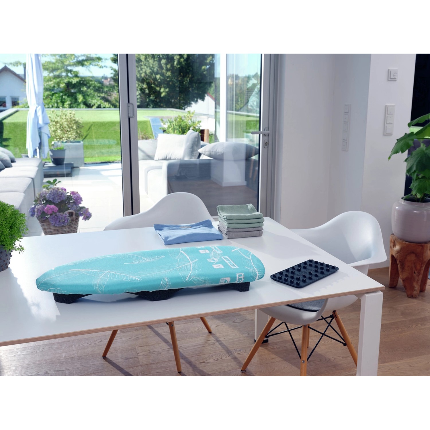 Leifheit AirBoard Compact Tischbügelbrett auf einem Tisch, mit Wäsche und Bügeleisenablage.