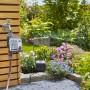 Gardena Bewässerungscomputer Master am Wasserhahn mit Gartenbewässerung im Hintergrund.