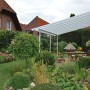 Weiße Palram Canopia Terrassenüberdachung Feria 4x6.06 im Garten mit Tisch und Stühlen.