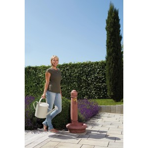 Garantia Steinbrunnen Venezia Redstone mit Frau und Gießkanne im Garten.