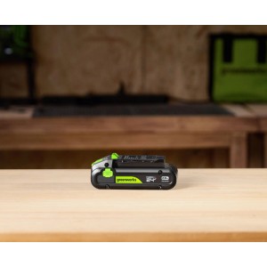 Greenworks 24V Akku 2Ah auf Holztisch. Schwarzer Lithium-Ionen-Akku mit grünen Details und 2.0Ah Kapazität.