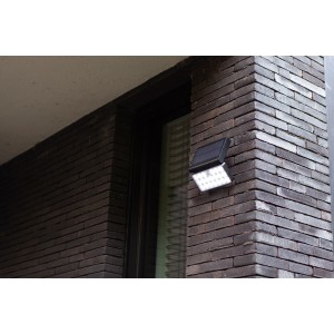 Schwarze LED Solar-Wandleuchte Tuda von Lutec mit Bewegungsmelder an einer Backsteinwand.