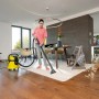 Frau reinigt Teppich mit gelbem Kärcher Waschsauger SE 4004 im Wohnzimmer.