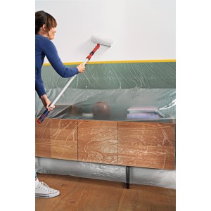 Frau streicht Wand mit Tesa Abdeckfolie Easy Cover Perfect+ XL, Möbel abgedeckt.