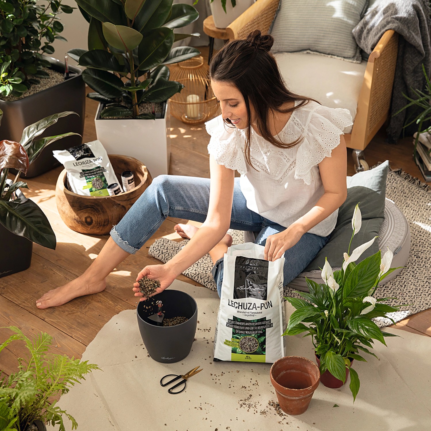 Frau befüllt Topf mit Lechuza-Pon Pflanzsubstrat. Zimmerpflanzen und Zubehör im Raum.