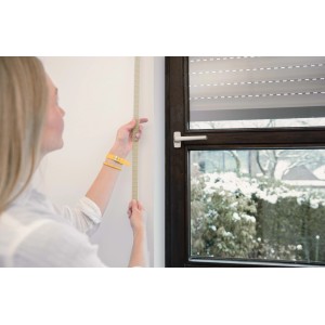 Frau misst mit beigem Schellenberg Rollladengurt Maxi die Fensterhöhe.