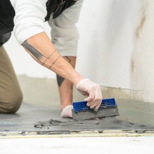 Handwerker verlegt Fliesen mit Mapei Fliesenkleber C2TE auf dem Boden.