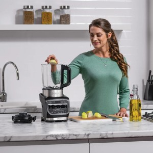 Frau gibt Zwiebel in Ninja Foodi Mixer & Suppenkocher. Küchenmaschine mit Glasbehälter.