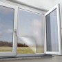 Anthrazitfarbenes Pollenschutznetz am Fenster, teilweise abgelöst, mit Blick nach draußen.