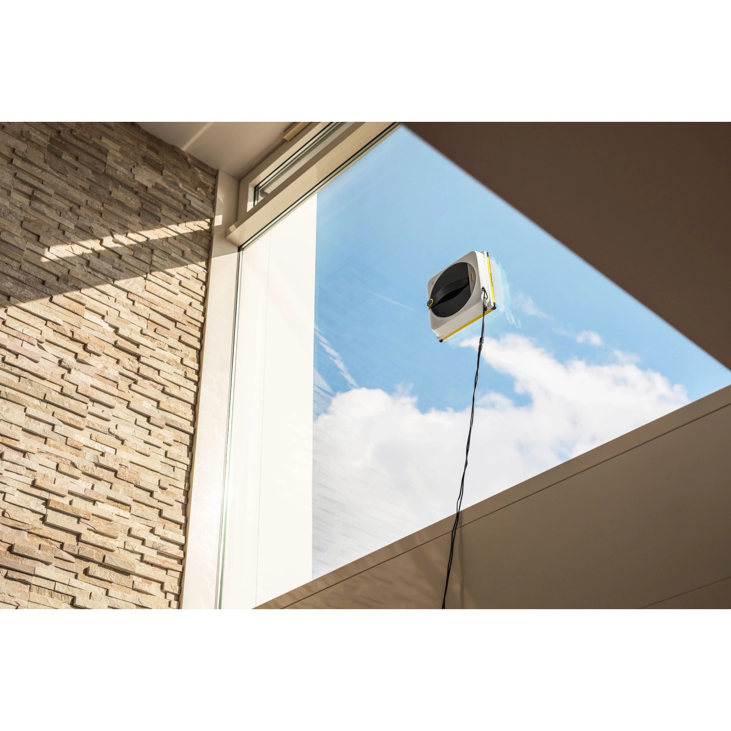 Kärcher RCW 4 Fensterputzroboter bei der Arbeit an einem Fenster mit blauem Himmel im Hintergrund.