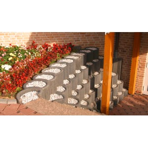 Graue Hangflor Pflanzsteine als Hangbefestigung mit Kies befüllt und Blumen im Hintergrund.