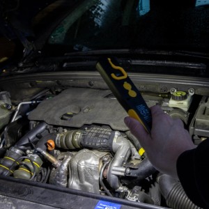 LED's Work Akku Handlampe leuchtet in einem Motorraum. Der LED-Baustrahler ist schwarz-gelb.