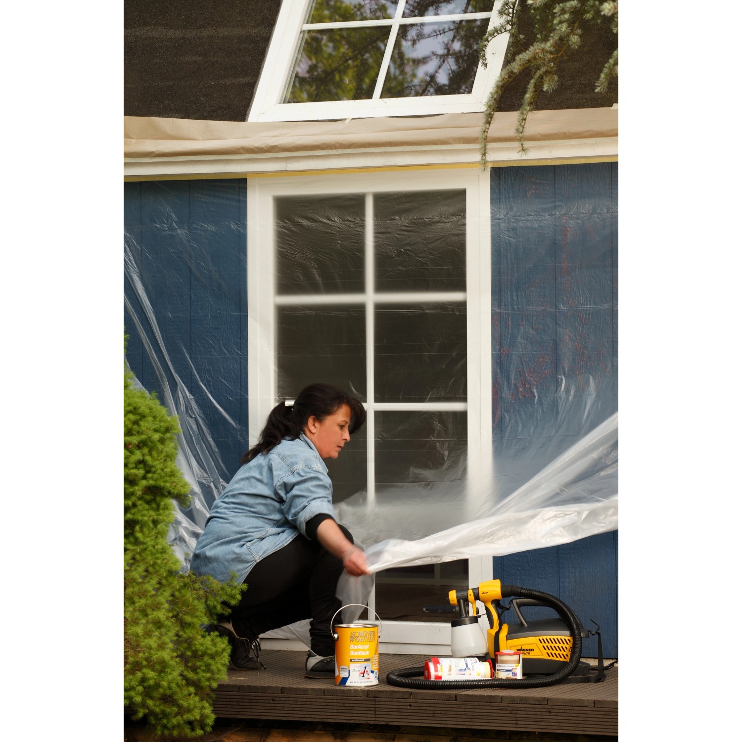 Frau deckt Fenster mit Tesa Easy Cover Universal Folie ab. Abdeckmaterialien für Renovierung.