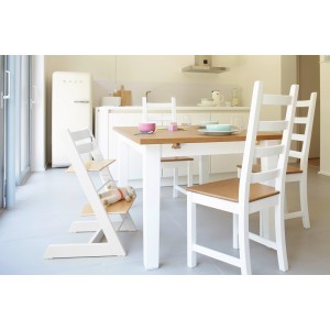 Esstisch mit weißen Beinen und Holzplatte, umgeben von weißen Stühlen und einem Kinderhochstuhl.