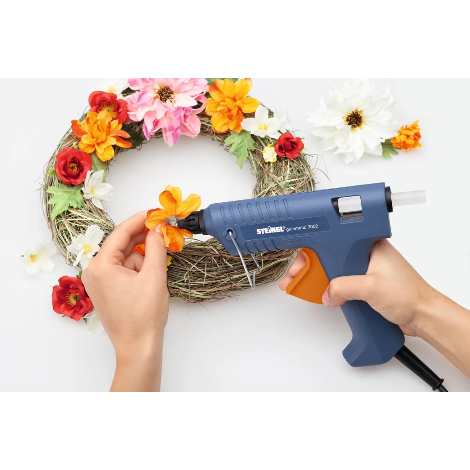 Steinel Heißklebepistole beim Anbringen von Blumen auf einem Kranz, mit transparenten Heißklebesticks.