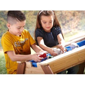 Kinder spielen am Axi Sand- und Wasser-Picknicktisch Nick (braun/blau/weiß) mit Sonnenschirm.
