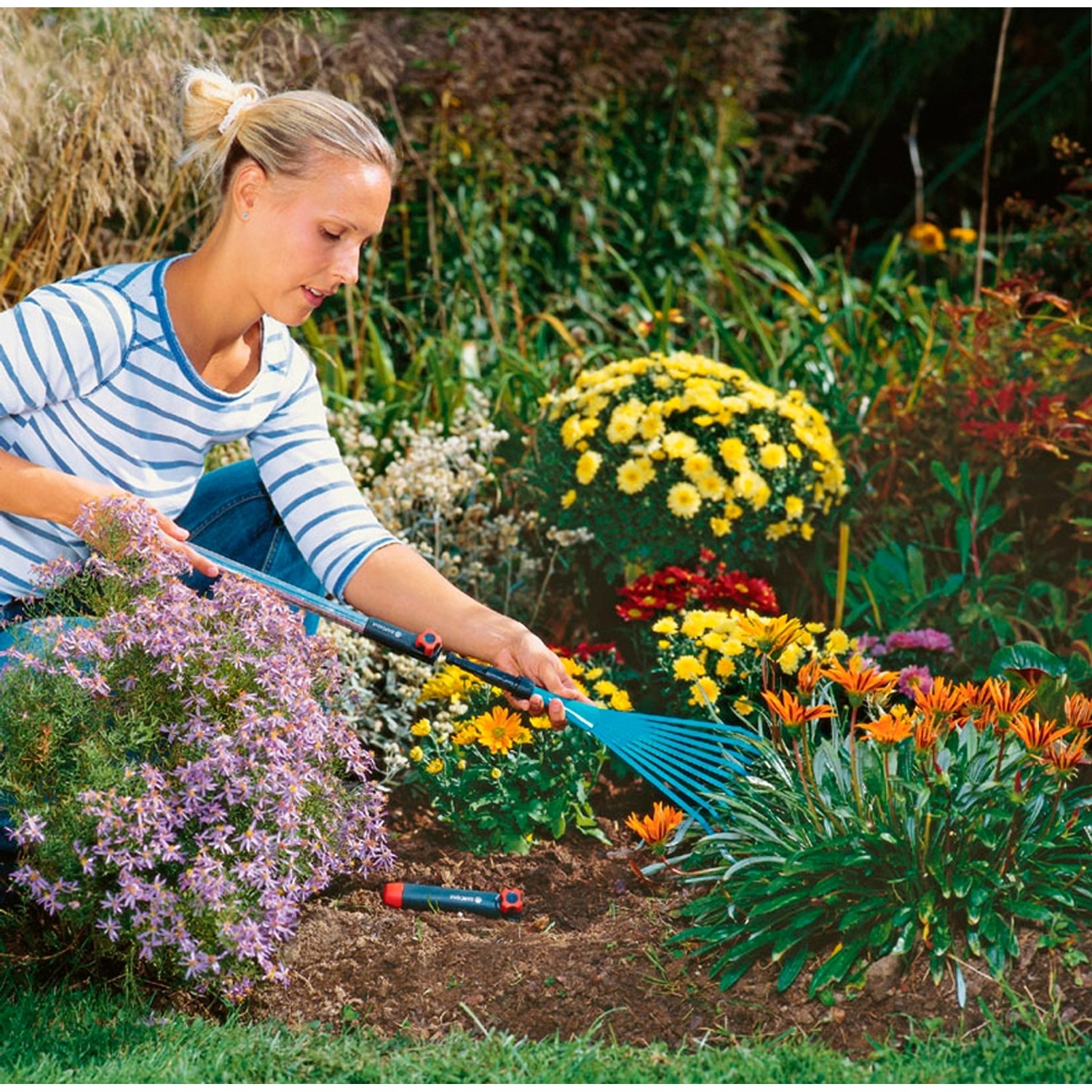 Frau arbeitet im Garten mit Gardena combisystem-Kleingeräte-Verlängerungsstiel 78 cm und Rechen.