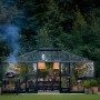 Juliana Gewächshaus Grand Oase 25 in Schwarz-Anthrazit mit Esstisch und Pizzaofen im Garten.