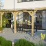 Skan Holz Terrassenüberdachung Andria aus Leimholz mit Polycarbonat-Dach auf Terrasse mit Tisch und Stühlen.