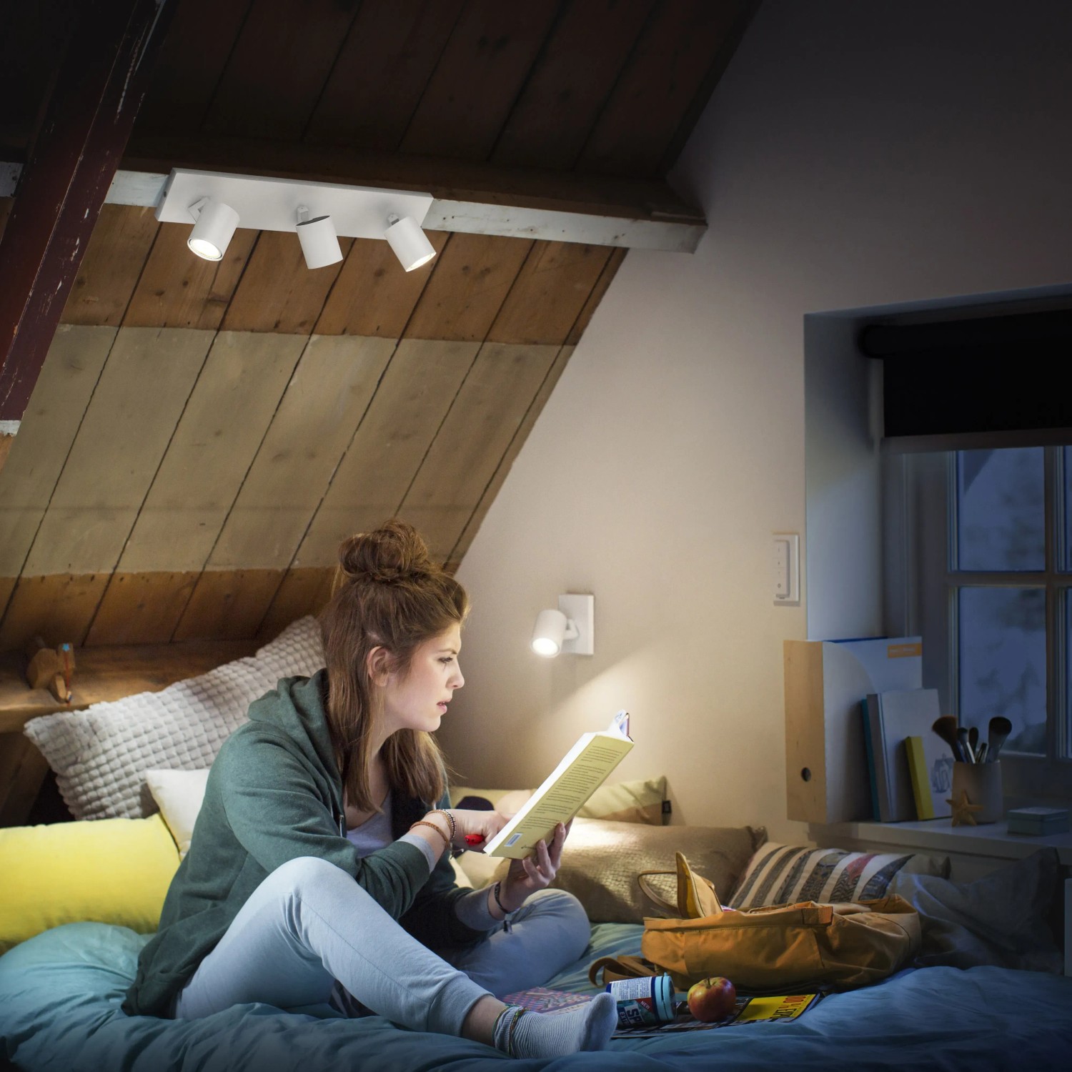 Philips Hue Runner, 3-flammig, Weiß: Frau liest im Licht der smarten Deckenleuchte im Dachzimmer.