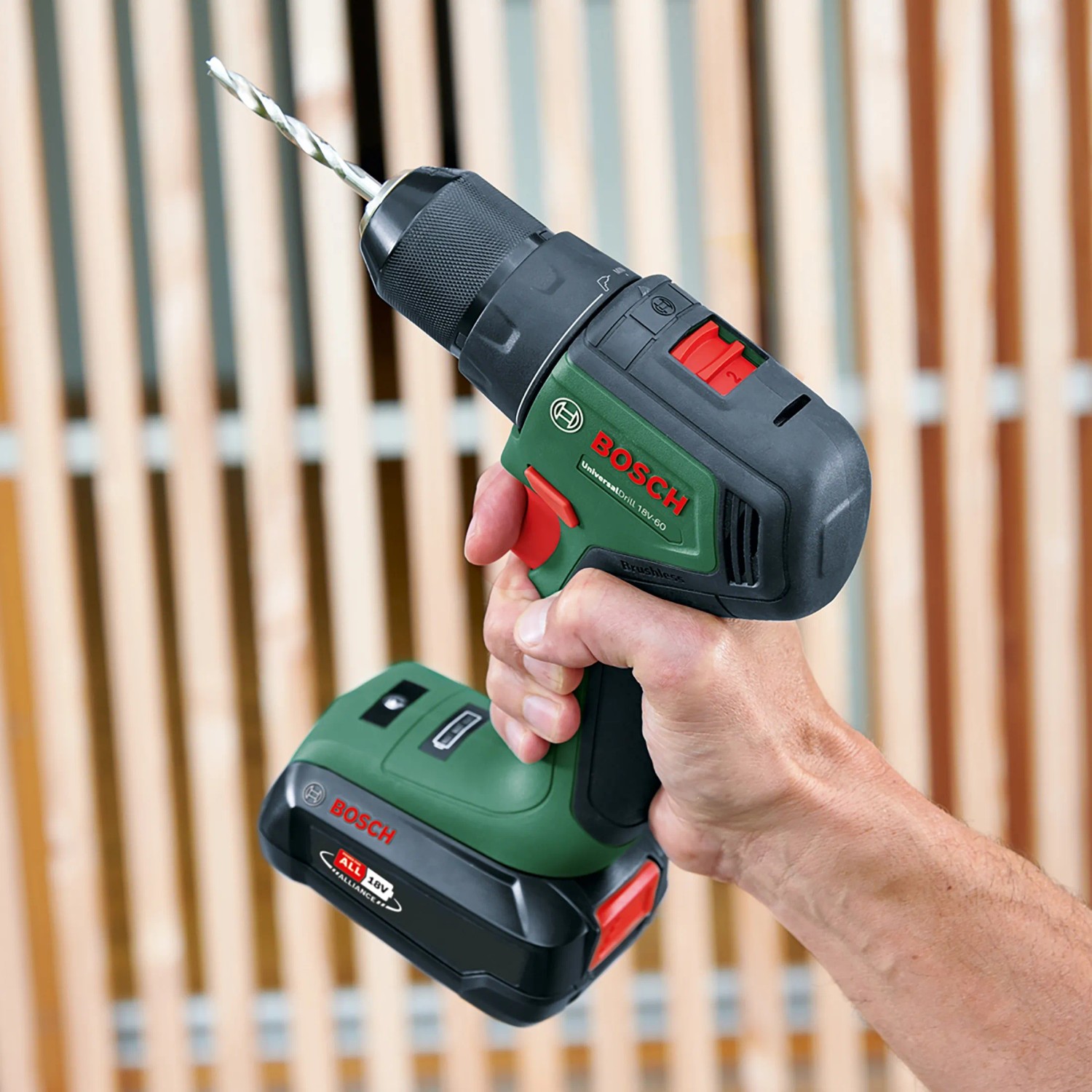 Bosch Akku-Bohrschrauber UniversalDrill 18V-60 Solo mit Bohrer in Hand vor Holzwand.