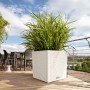 Weißer Lechuza Cube Cottage Pflanzkübel (50x50x50 cm) mit Pflanze auf einer Terrasse.